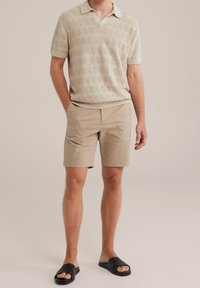 Beige knitted polo shirt with a textured honeycomb pattern, paired with light khaki shorts and black slides.