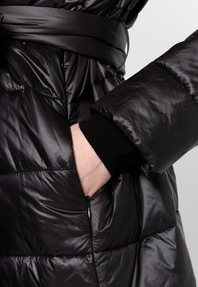 Czarna kurtka puchowa z elegancką, błyszczącą teksturą, pikowanym wzorem, paskiem w talii i dzianinowymi mankietami. Widoczna boczna kieszeń z zamkiem.