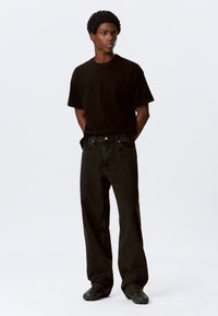 Black cotton t-shirt paired with loose-fitting, dark denim jeans. The outfit features a relaxed fit and subtle stitching details.