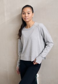 Lys grå kort sweatshirt laget av mykt stoff, med rund hals, sidespalter og ribbestrikkede mansjetter, kombinert med svarte leggings.