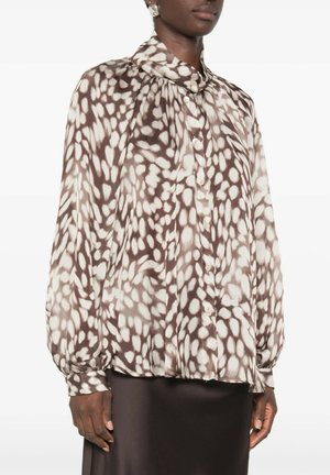 Vrouw draagt een losse blouse met lange mouwen en knopen met bruine en witte abstracte vlekken, gecombineerd met een zwarte rok.