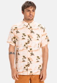 Korte mouw knopshirt van een licht perzikachtige stof met palmboom- en eilandsgrafieken, met contrasterende tekst en een relaxte pasvorm.