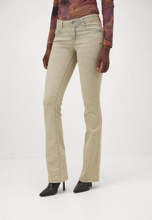 Beige flared jeans with a mid-rise waist, featuring front pockets and slim fit through the hips, paired with pointed black high heels.