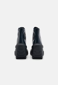 Černé, lesklé boty po kotníky s texturovaným povrchem a logem, s robustní podrážkou a vzorovaným gumovým dnem.