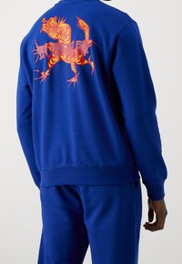 Sudadera azul con cuello redondo que presenta un gráfico vibrante de un tigre naranja en la espalda, hecha de una suave mezcla de algodón.