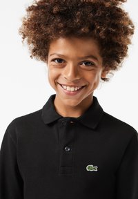 Black polo shirt made of textured fabric with a collar, two button placket, and a green embroidered crocodile logo on the chest.