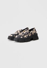 Plátěné slip-on boty s potiskem kravské kůže v béžové a černé barvě, s robustní černou gumovou podrážkou a zlatými kovovými detaily.