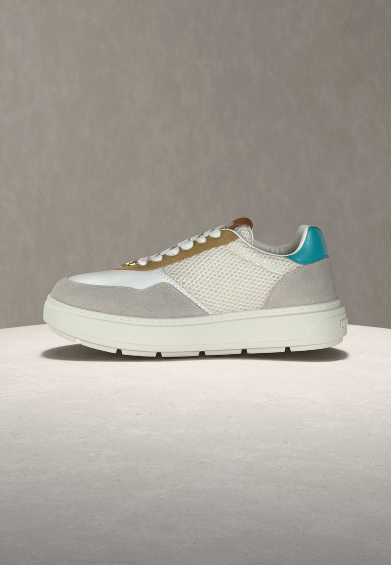 Λευκό και μπεζ αθλητικό παπούτσι με πάνελ από δίχτυ και σουέντ, λευκά κορδόνια, καφέ διακριτικό κοντά στη γλώσσα και τιρκουάζ ταμπελάκι στη φτέρνα, τοποθετημένο σε ανοιχτή επιφάνεια.