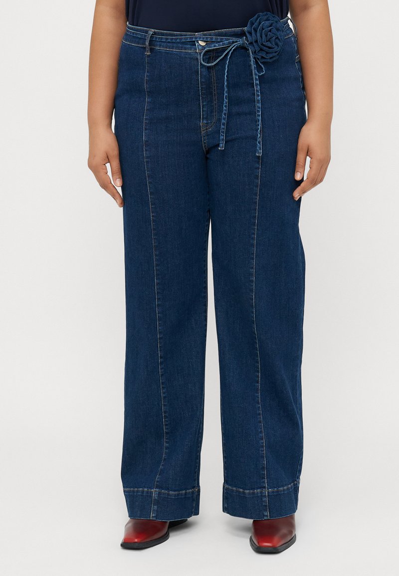 Szerokie dżinsowe spodnie w ciemnoniebieskim kolorze, z kwiecistym detalem paska, wykończone klasycznym pięciomapowym wzorem i kontrastowym przeszyciem.