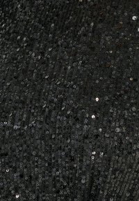 Svart tyg täckt av tätt packade, glänsande paljetter, som skapar en texturerad yta med varierande ljusreflektioner och mönster.