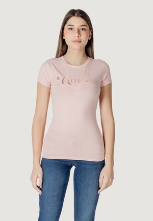 T-shirt fitted rosa chiaro realizzato in morbido cotone, con un logo "Guess" luccicante sul davanti, abbinato a jeans blu.