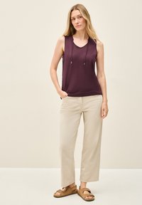 Haut sans manches violet avec un décolleté en V et un détail de cordon, associé à un pantalon beige à jambes larges et des sandales à glissière marron.