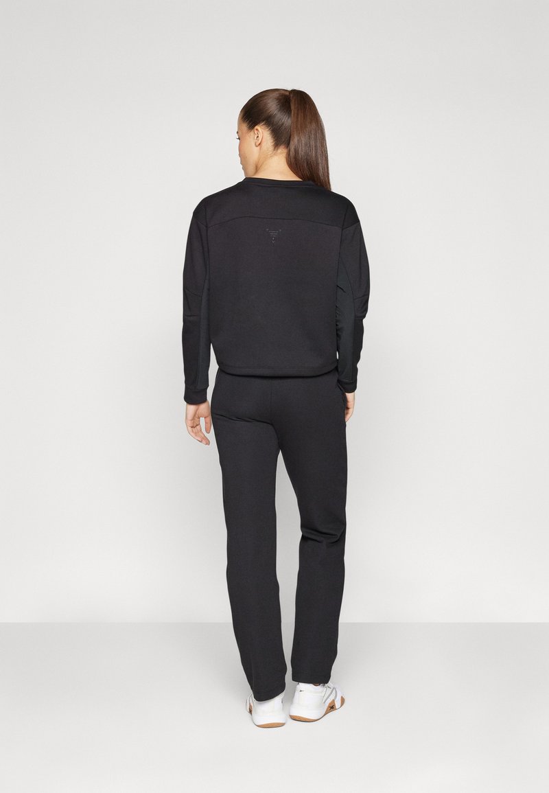 Completo activewear nero che include una felpa aderente e pantaloni, realizzati in materiale morbido. La parte superiore presenta un discreto dettaglio con logo e polsini a coste.