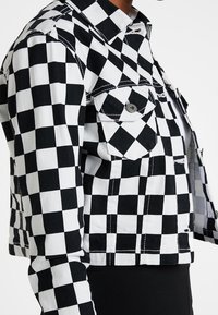 Svartrutig denimjacka med en krage, två framfickor och synliga sömmar; kort längd, texturerat tyg.