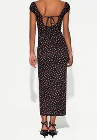 Robe midi noire avec motif floral rose, manches courtes bouffantes, dos nu avec détail à nouer et coupe ajustée. Accentuée avec des talons à lanières.