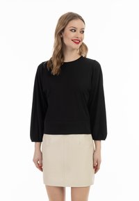 Sort pullover med lange ballonærmer, rund hals og tætsiddende kant. Båret med en beige mini-nederdel, der fremviser en glat tekstur og enkelt design.