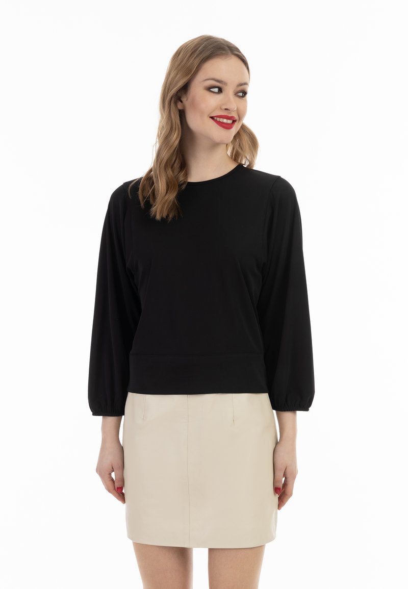 Sort pullover med lange ballonærmer, rund hals og tætsiddende kant. Båret med en beige mini-nederdel, der fremviser en glat tekstur og enkelt design.