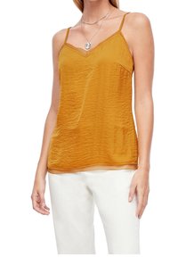 Camisole couleur ambre avec des bretelles spaghetti réglables, tissu texturé et dentelle au niveau de l'ourlet du décolleté. Associée à un pantalon blanc.