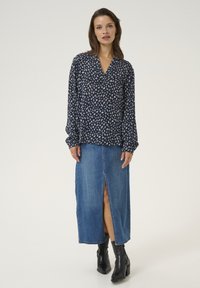 Marinblus med bladmönster, lång ärm och V-ringning, tillsammans med en denimkjol med pennform som har en slits framtill och svarta ankelboots.