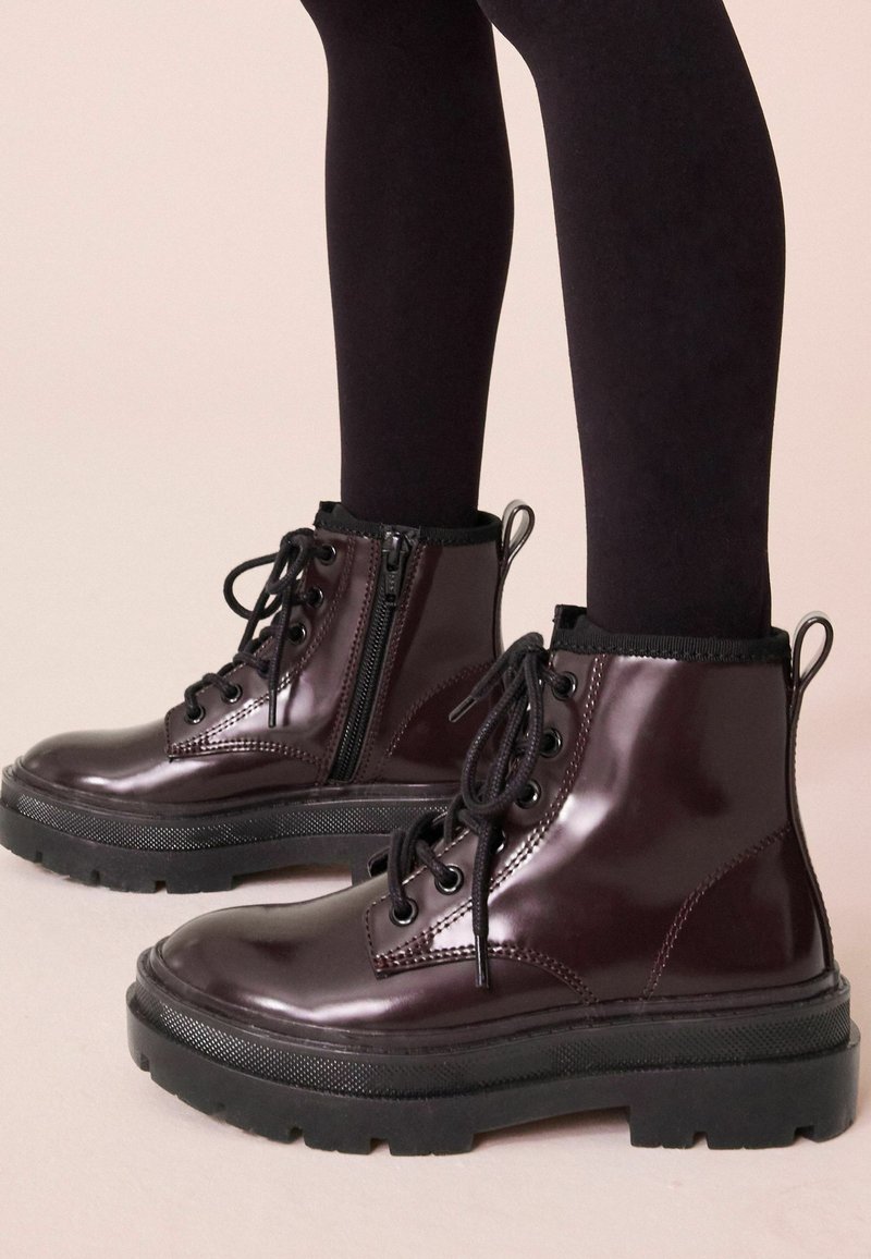 Bottes de cheville en cuir verni bordeaux avec bouts ronds, semelles en caoutchouc noir, devant à lacets et détail de fermeture éclair sur le côté. Col élastique noir.
