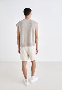 Beige strikket ermeløs topp med ribbestrikket kant, kombinert med lyse linshorts. Modellen har på seg hvite joggesko og sokker.