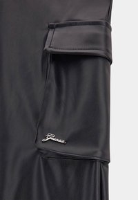 Svart läderjacka med en strukturerad yta, manschettdetaljer och en silverfärgad "Guess"-logotyp på framsidan.