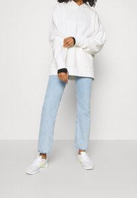 Felpa oversize bianca con polsini neri, jeans a gamba dritta blu chiaro e sneakers bianche con dettagli gialli.