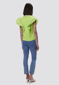 Top verde lime con maniche a volant, abbinato a jeans skinny azzurri chiari, presenta una lunghezza cropped e orlo sfrangiato. Sandali semplici completano il look.