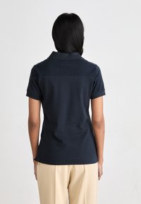 Πόλο μπλούζα με κοντό μανίκι σε ναυτικό μπλε χρώμα. Κατασκευασμένη από βαμβάκι με κλασικό γιακά και κυλιόμενα μανίκια. Λεπτή υφή, απλός σχεδιασμός και λεπτομέρεια ραφής στην πλάτη.