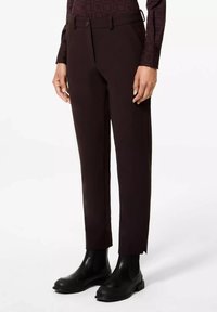 Pantalon sur mesure marron foncé avec une texture lisse, passants de ceinture et fermeture à bouton unique, associé à des bottes noires à talons épais.