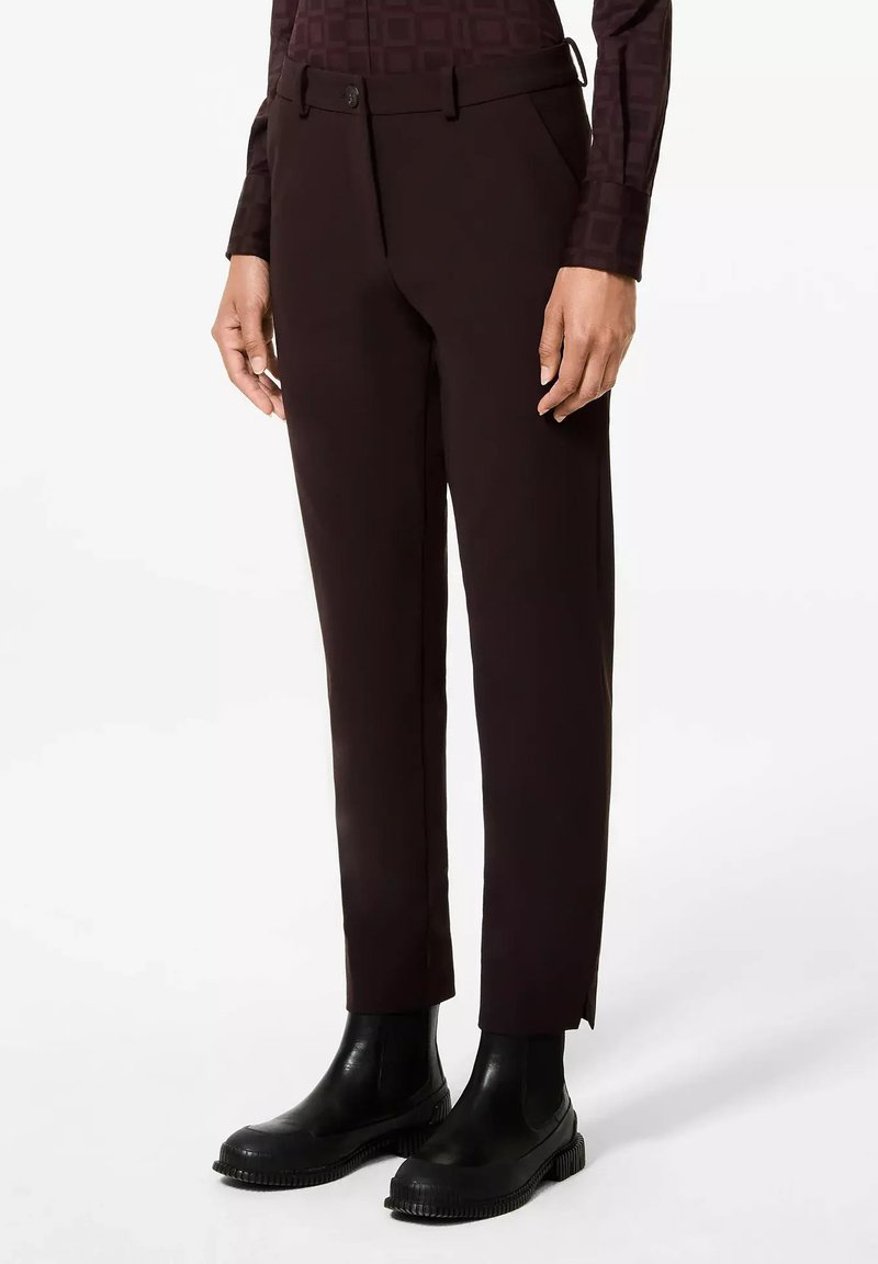 Pantalon sur mesure marron foncé avec une texture lisse, passants de ceinture et fermeture à bouton unique, associé à des bottes noires à talons épais.