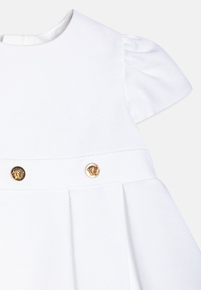 Hvit kjole med korte puffede ermer, plissert skjørt og to gullløvehodeknapper. Laget av teksturert stoff, som gir et strukturert utseende.