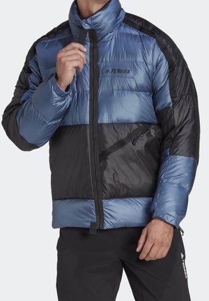 Homme portant une veste matelassée Terrex bleue et noire, fermeture éclair partiellement fermée, avec un pantalon Terrex noir.