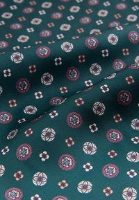 Green fabric with a smooth texture, featuring a repeated pattern of intricate floral and circular designs in red, white, and blue.
