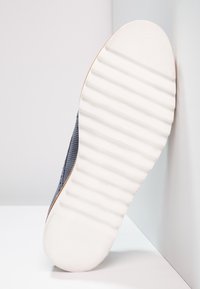 Sneaker in rete blu scuro con suola in gomma bianca testurizzata, mostra un motivo rigato e punta arrotondata; branding discreto sulla suola.