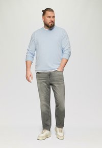 Hellblaues Langarmhemd kombiniert mit grauen Jeans und beigen Sneakers. Der Stoff wirkt weich und die Jeans haben eine ausgebleichte Textur.