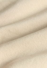 Beiger Stoff mit glatter Textur, der ein feines Strickmuster aufweist. Das Material wirkt weich und leicht, mit sanften Falten und einem fallenden Fall.