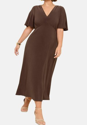 Femme portant une robe midi marron à col en V avec de courtes manches volantées, des sandales beiges à brides, un bracelet en or et des boucles d'oreilles créoles jaunes.