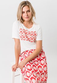 Korte mouwen witte T-shirt met een geometrisch rood en wit patroon op de voorkant, gecombineerd met een bijpassende rok met hetzelfde patroon. Soepele stof.
