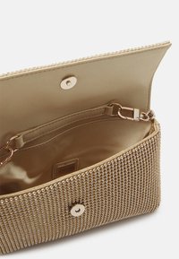 Metalni zlatni clutch sa zasićenom površinom od malih šiljaka. Unutrašnjost sadrži satenasto oblaganje i pričvršćenje za lančić. Zatvaranje na klik.