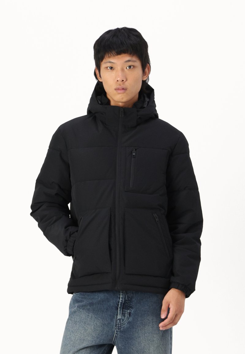 Chaqueta acolchada negra con capucha, cremallera frontal y bolsillos laterales. Cuenta con un bolsillo en el pecho con cremallera, diseñado para brindar calidez y comodidad.