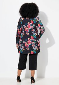 Zwarte bloemen tuniek met lange mouwen, versierd met meerkleurige bloemen. Gecombineerd met zwarte cropped broek en zwarte hakken. Soepele textuur.