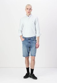 Lys blåstripet skjorte, denimshorts, svarte sokker og joggesko. Antrekket har en uformell stil med vanlig passform og enkle detaljer.