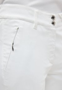 Λευκό παντελόνι με φερμουάρ σε πλαϊνή τσέπη, διπλά μαύρα κουμπιά με τρουκ και θηλιές για ζώνη, φορεμένο με λευκή ριμπ μπλούζα.