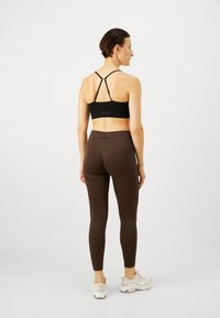 Barna, magas derekú leggings, finom textúrával, fekete, pántos sportmelltartóval párosítva. A stílus minimalista, logóval kiemelve.