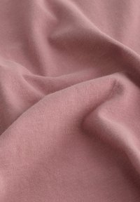 Țesătură moale, texturată, într-o nuanță roz pal, care prezintă pliuri și curbe delicate, cu un model fin de tricot pe întreaga suprafață.