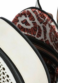 Sac à dos en simili cuir blanc avec fermeture éclair noire et design perforé. L'intérieur présente un tissu à motifs dans des tons orange et marron avec du texte.