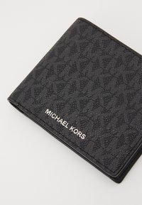 Portefeuille en cuir noir avec motif logo gaufré, arborant une marque argentée "MICHAEL KORS" à l'extérieur, dans un design bi-fold.