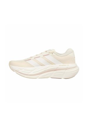 Chaussure de course beige clair avec des accents blancs et rose pâle, semelle épaisse et rembourrée, et trois bandes blanches sur le côté.