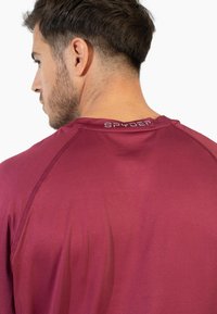 Bordeaux performance top med raglanærmer, glat tekstur og SPYDER-logo ved halsen. Let stof til aktiv sport.